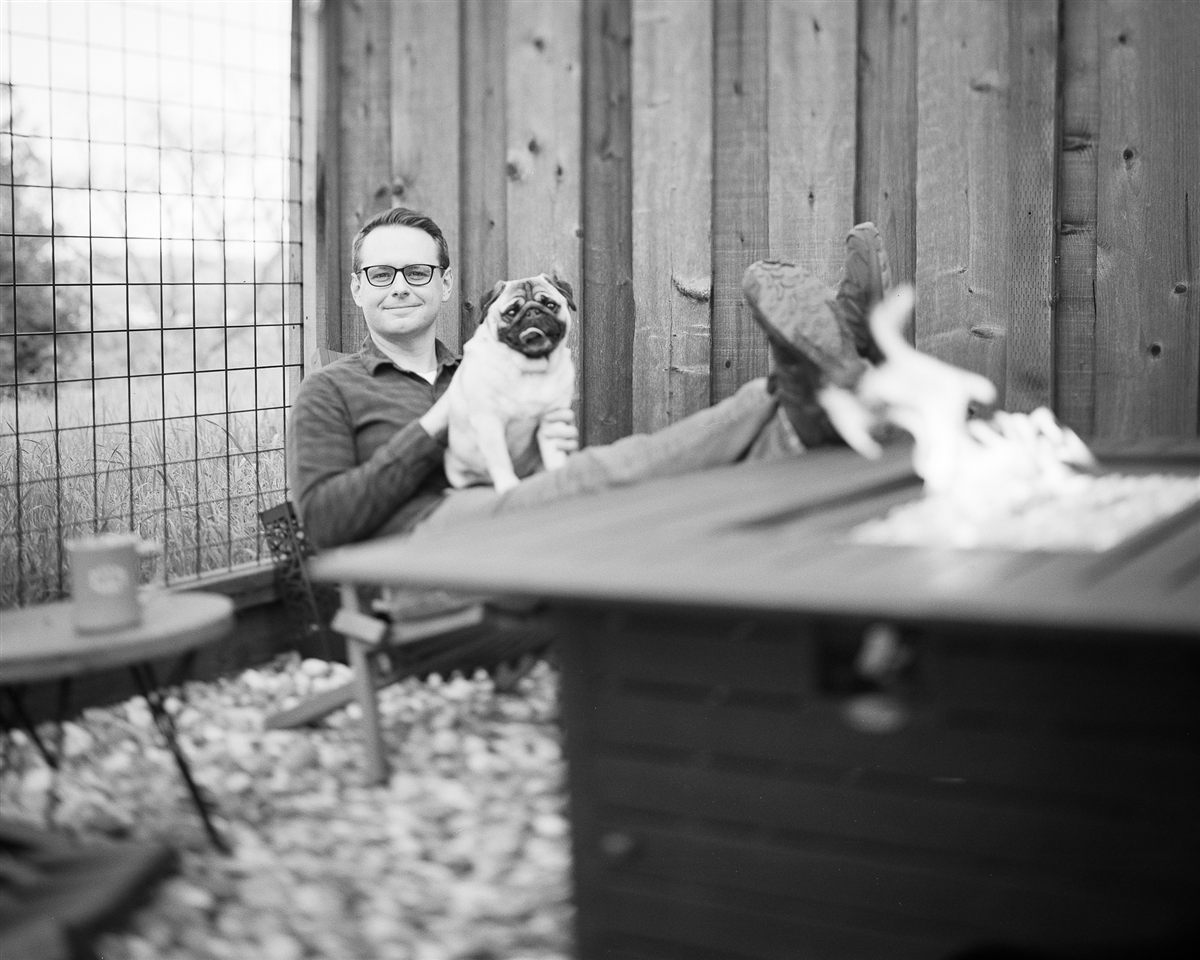 Justin Parnell sitting beside a fire pit with his pug